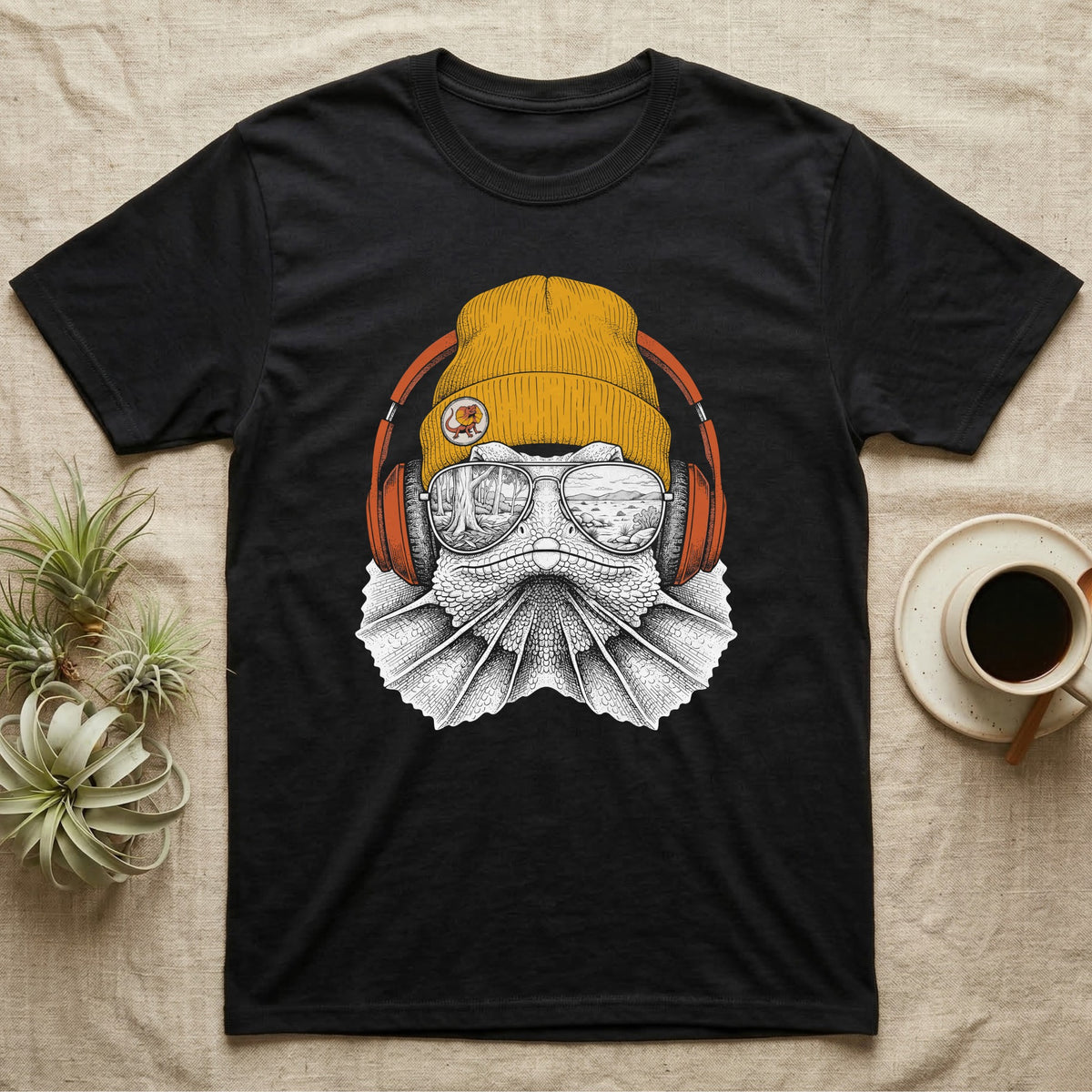 Frilled Lizard Headphones T-Shirt in Black — Engraved frilled lizard with fanned frill in a beanie and headphones, aviators reflecting savannah woodland.