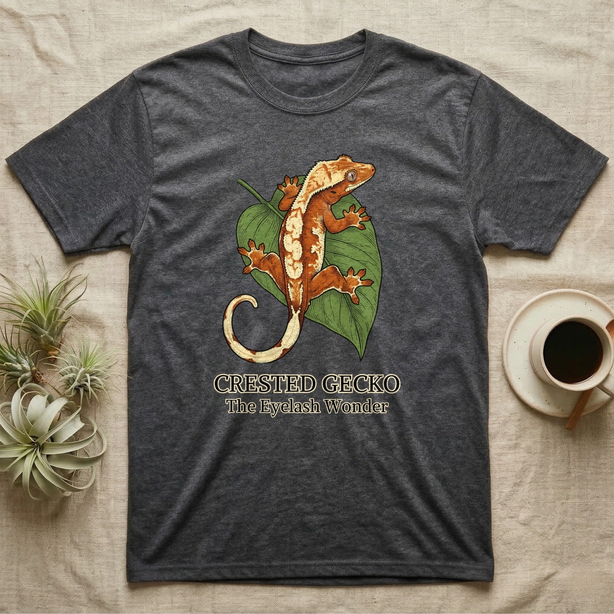 Dark grey t-shirt with a crested gecko and leaf graphic and text.