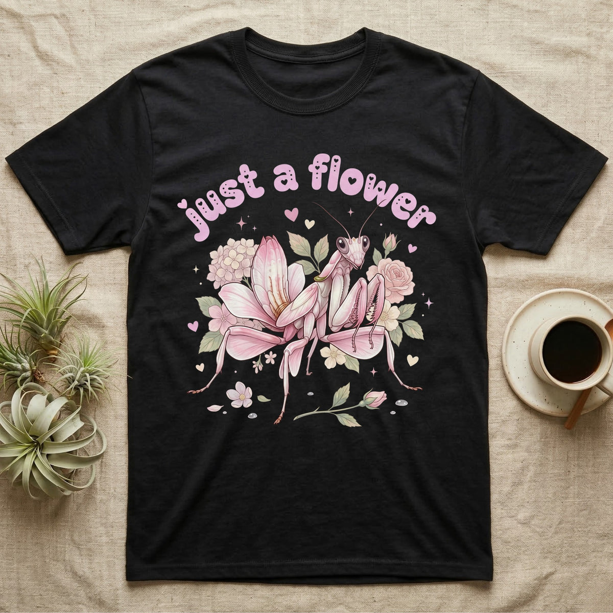 Orchid Mantis Softie T-Shirt in Black — Pink orchid mantis mimicking a flower under pastel bubble text "just a flower" with tiny hearts.