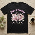 Orchid Mantis Softie T-Shirt in Black — Pink orchid mantis mimicking a flower under pastel bubble text "just a flower" with tiny hearts.