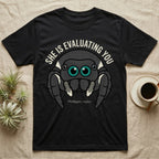 Phidippus Regius Jumping Spider Tee in Black — Vector-bold front-facing regal jumping spider portrait with electric-teal anterior-median eyes on a cream-and-charcoal body.