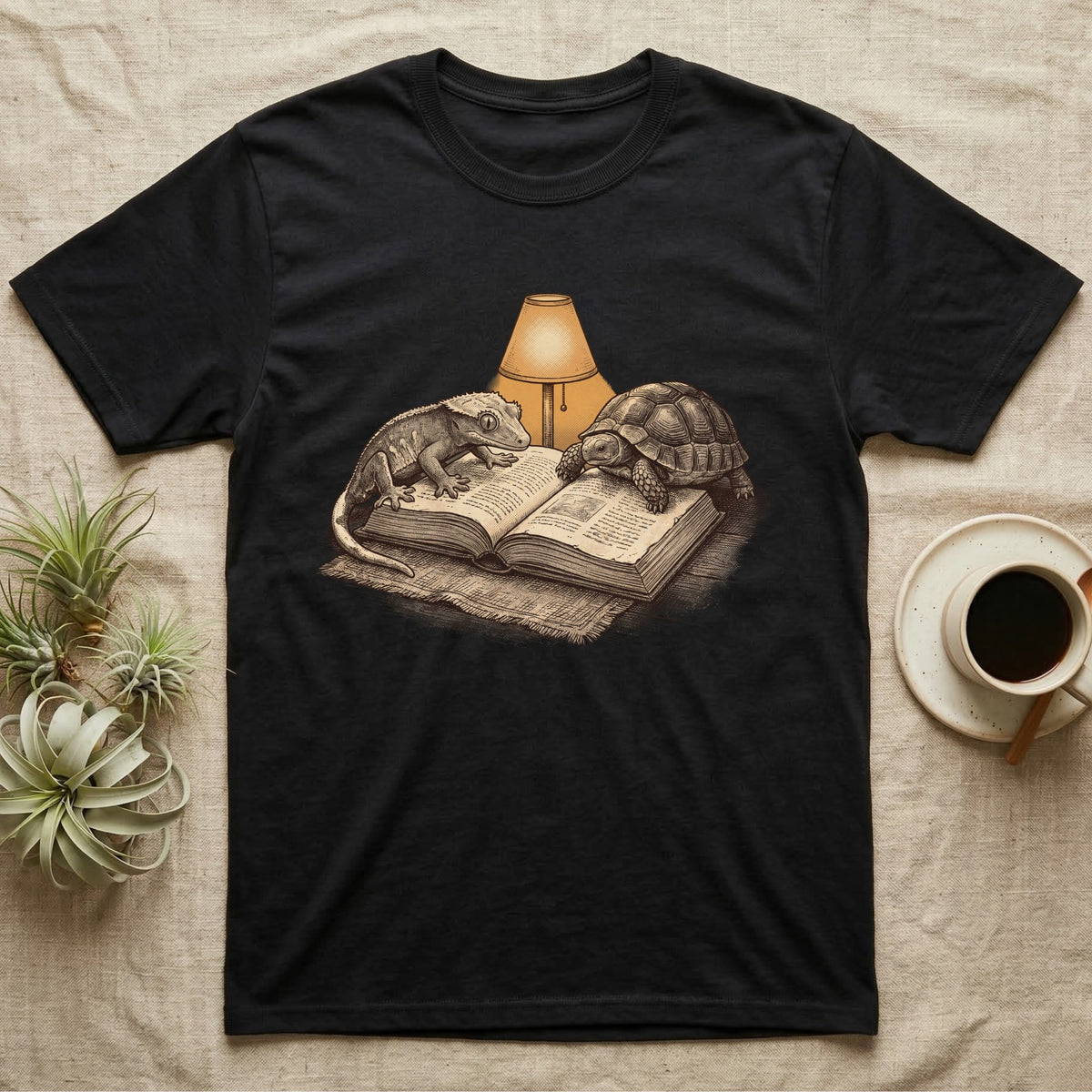 Cold-Blooded Book Club T-Shirt in Black — Engraved cozy illustration of a gecko and a tortoise sharing an open book under a glowing reading lamp.