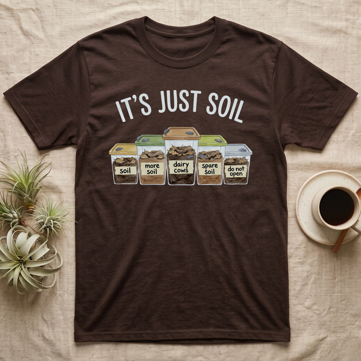 Isopod Soil Bins T-Shirt in Dark Chocolate — Watercolour row of five labelled bins of soil with isopods on the lids under the words IT'S JUST SOIL