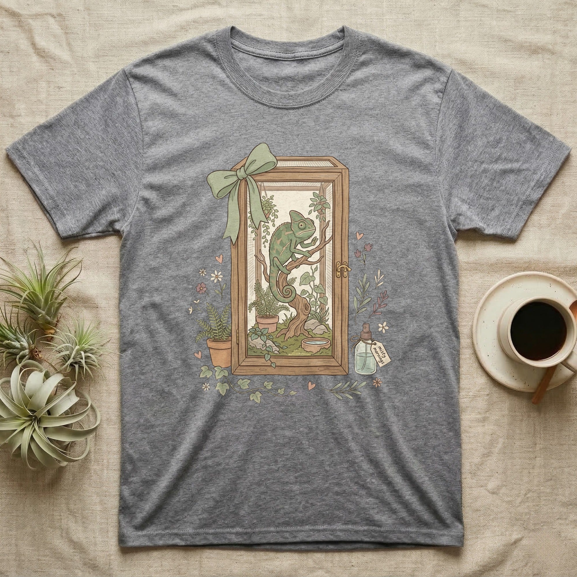 Chameleon in terrarium with plants, framed by a bow, on a grey t-shirt.