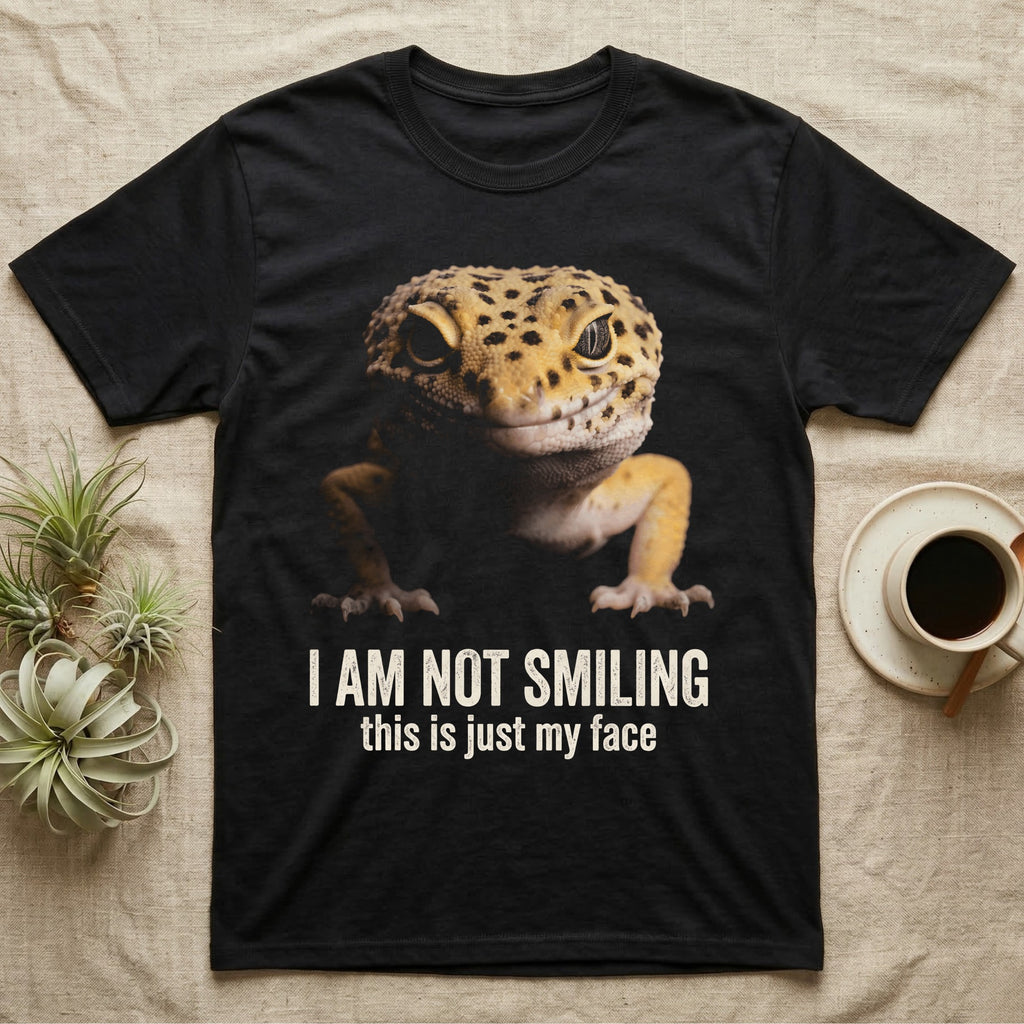 Photographic mugshot of a leopard gecko braced low and staring into the lens above the hook I Am Not Smiling, this is just my face. — shown on a Black tee.