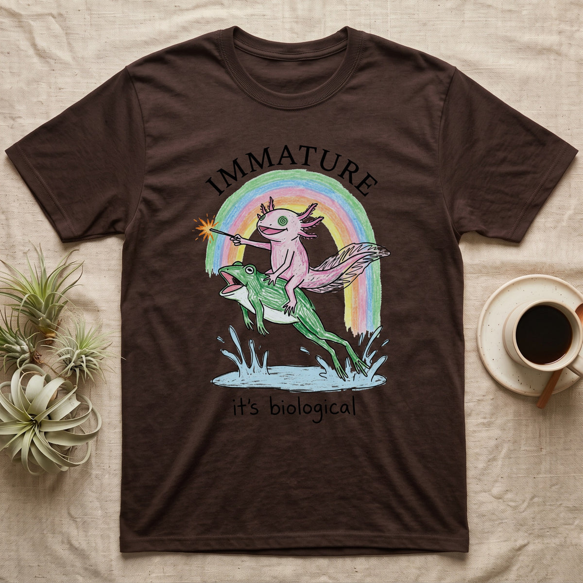 Axolotl Immature T-Shirt in Dark Chocolate — Crayon drawing of a pink axolotl riding a leaping green frog through a rainbow, sparkler lit, under IMMATURE