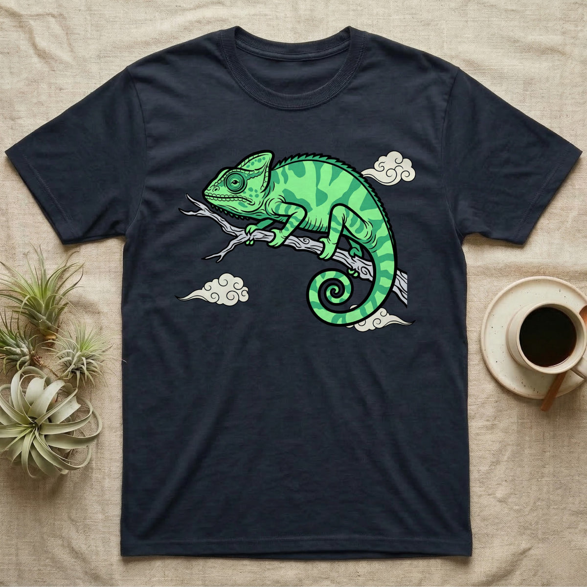 Dark t-shirt with a green chameleon on a branch, surrounded by clouds.