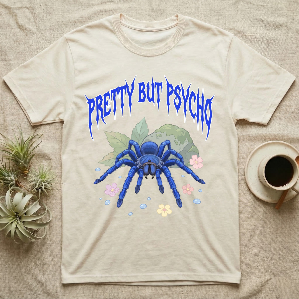 Cobalt Blue Tarantula Feral T-Shirt in Natural — Cobalt blue tarantula with electric-blue legs under jagged cobalt metal text PRETTY BUT PSYCHO with pastel blossoms