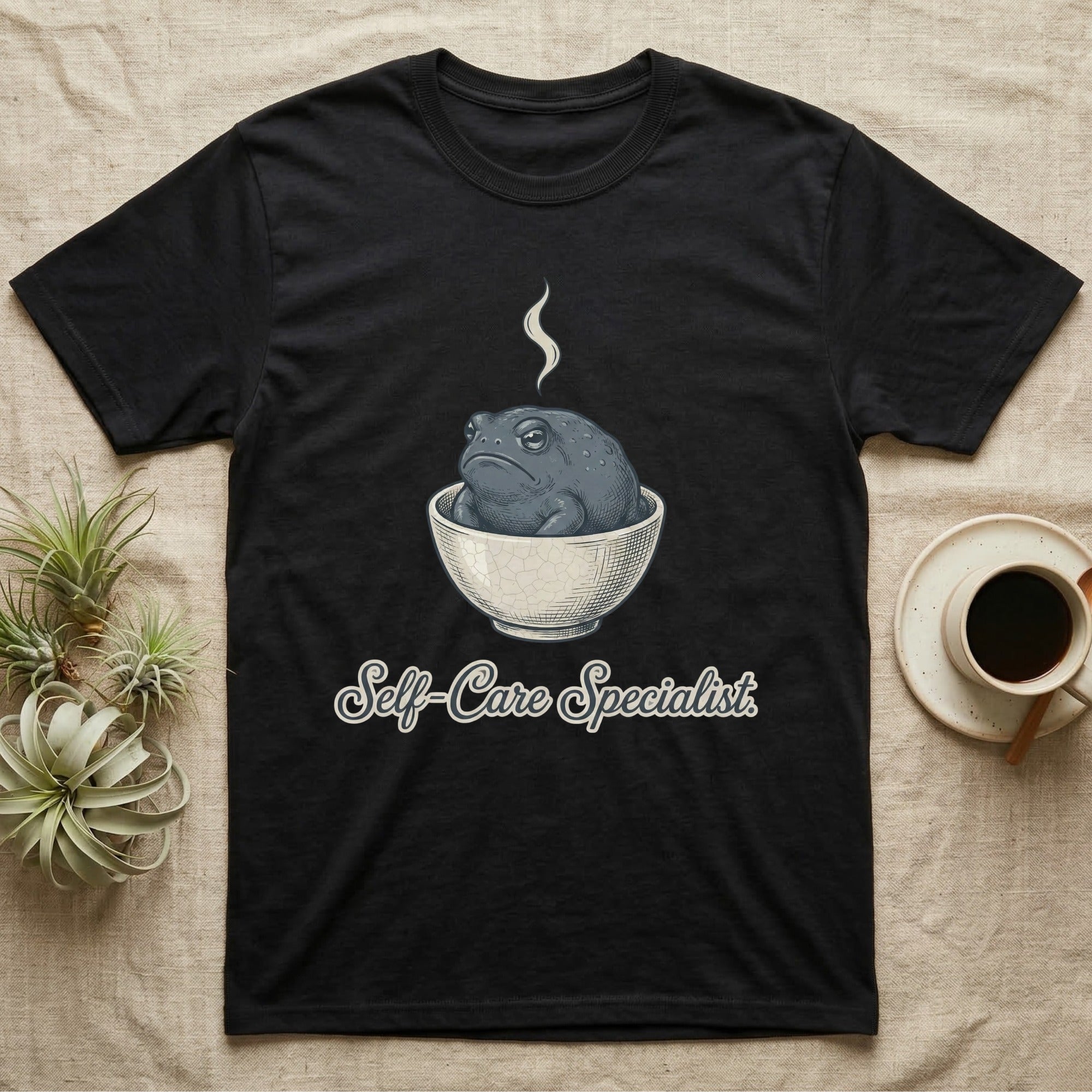Black t-shirt with a grumpy toad in a bowl, steaming, and "Self-Care Specialist" text.