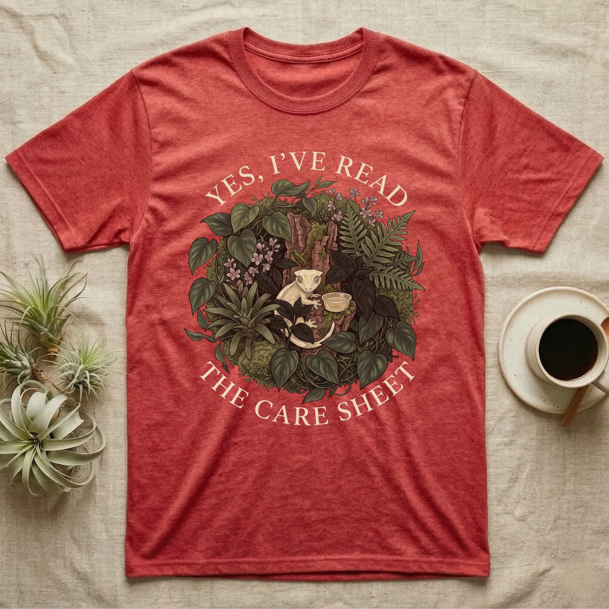 Crested Gecko Care Sheet T-Shirt in Heather Red — Botanical wreath of pothos and moss circling a crested gecko, closed by two arcs of Roman capitals.