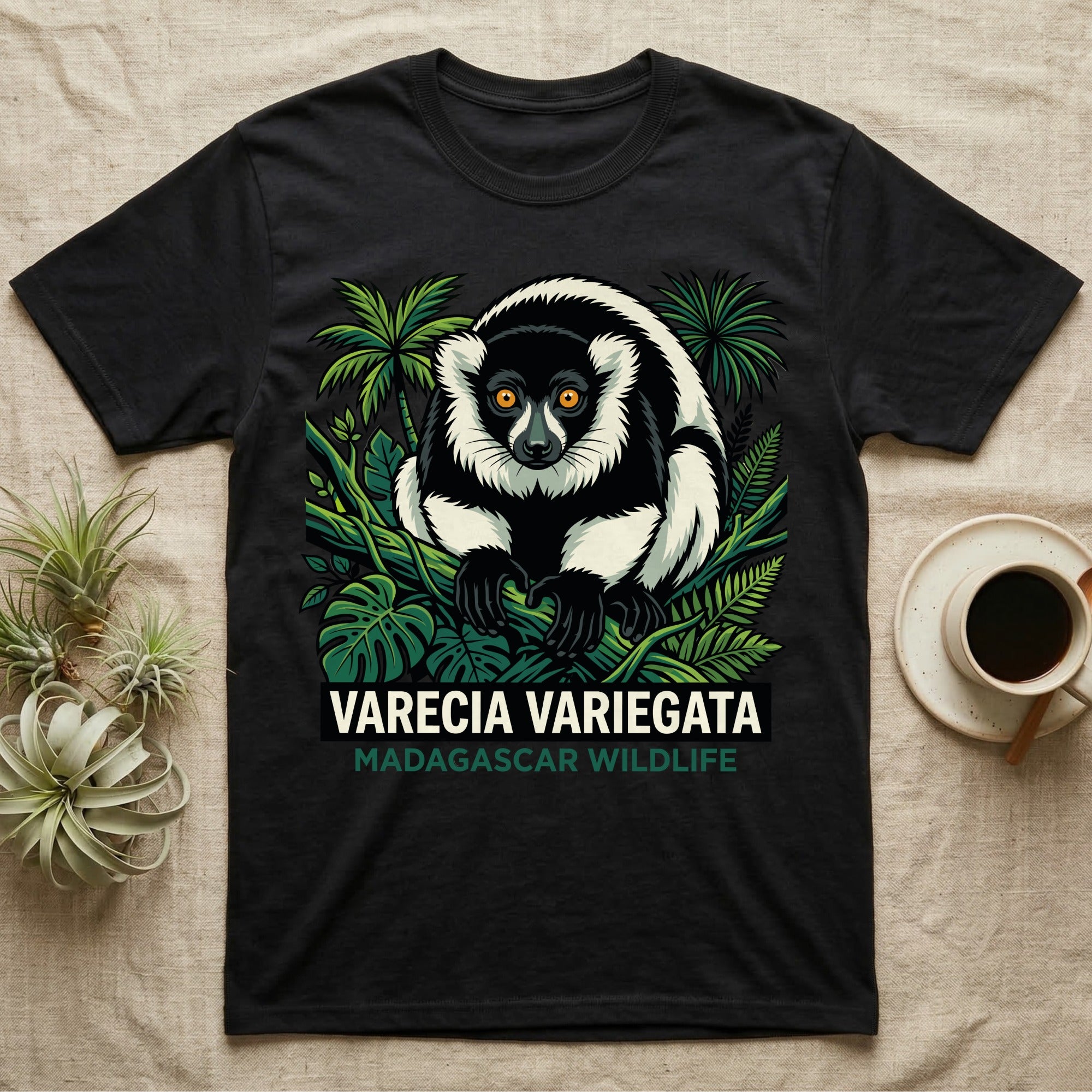 Black t-shirt with a varecia variegata lemur illustration surrounded by tropical leaves.