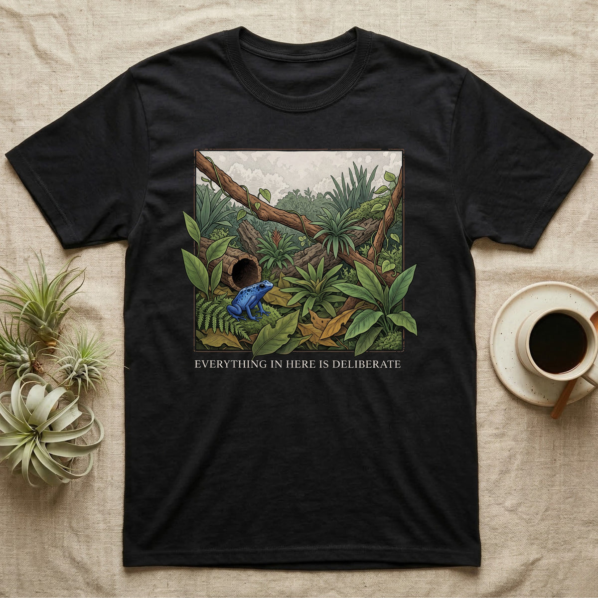 Dart Frog Bioactive Vivarium T-Shirt in Black — Illustrated panel of a cobalt dart frog in a layered planted vivarium, leaves crossing the inked border.