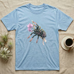 Pink-Toe Tarantula Blossom T-Shirt in Light Blue — Watercolor illustration of a charcoal pink-toe tarantula with salmon toe tips holding an orchid blossom sprig, on a dark grey t-shirt.