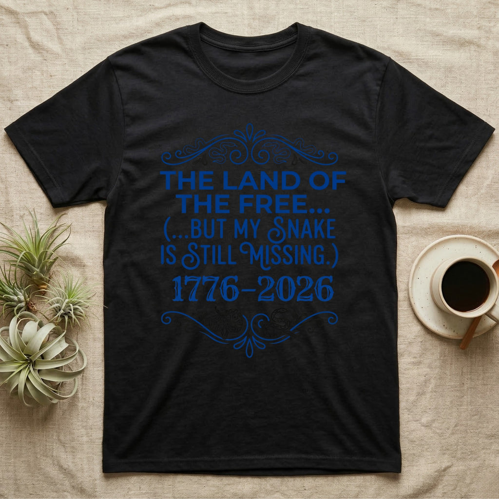 Corn Snake Still Missing Tee in Black — Royal blue typographic tee reading The land of the free but my snake is still missing, with Victorian filigree and small coiled corn snakes.