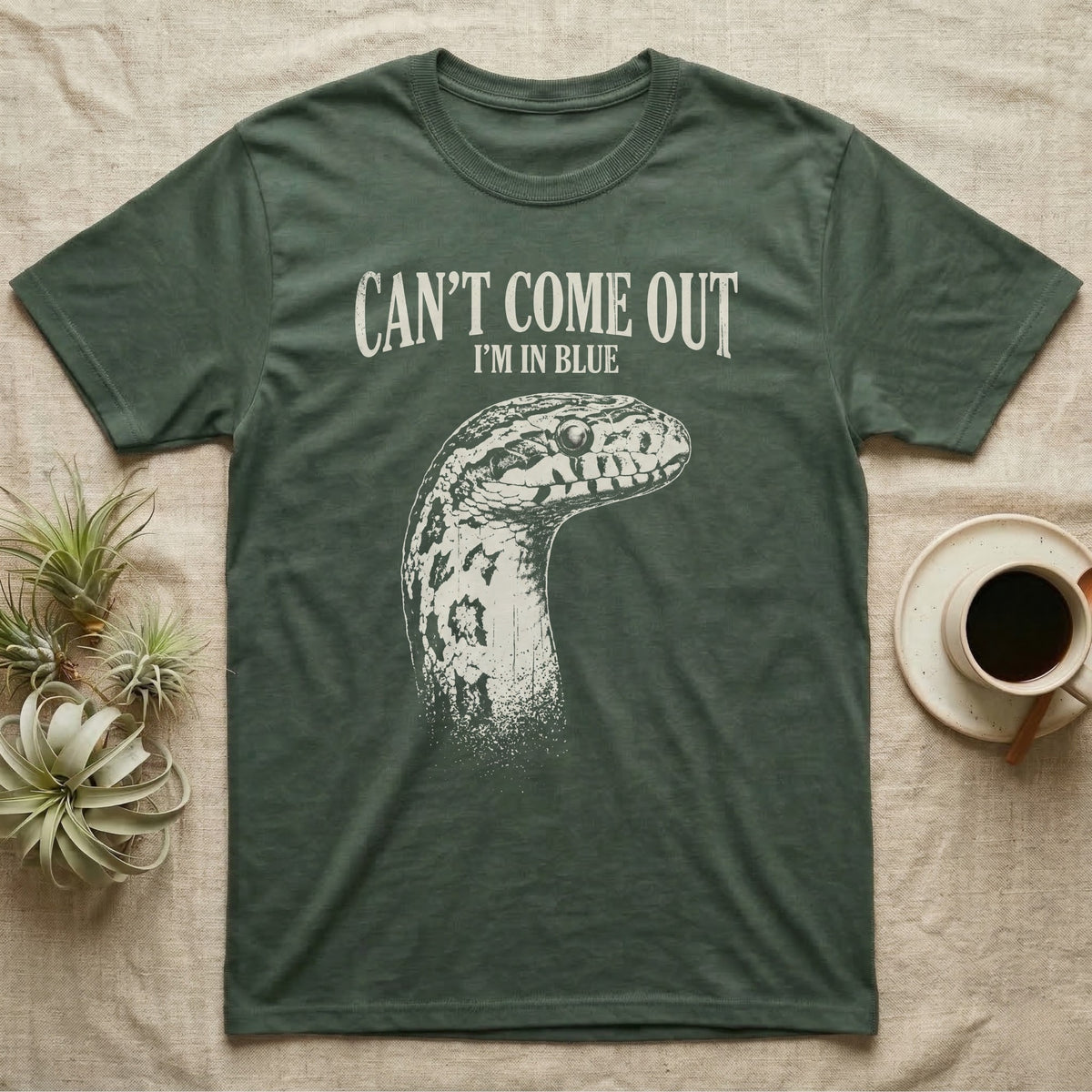 Corn Snake Shed T-Shirt in Military Green — Gritty white print of a corn snake head with milky pre-shed eyes under CAN'T COME OUT, I'M IN BLUE, on black