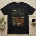 Corn Snake Home Range T-Shirt in Black — Woodcut-style illustration of a corn snake winding across pine straw beside a split log with pine trees behind, no on-shirt text.