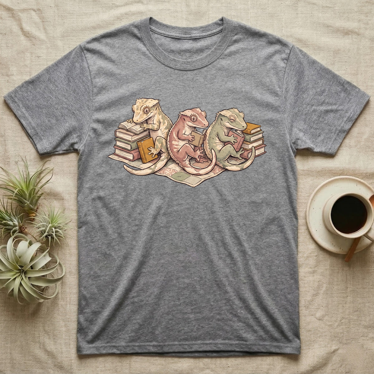 Gecko Book Club T-Shirt in Sport Grey — Warm storybook illustration of three crested geckos in a cozy reading row, each beside a tiny stack of books.