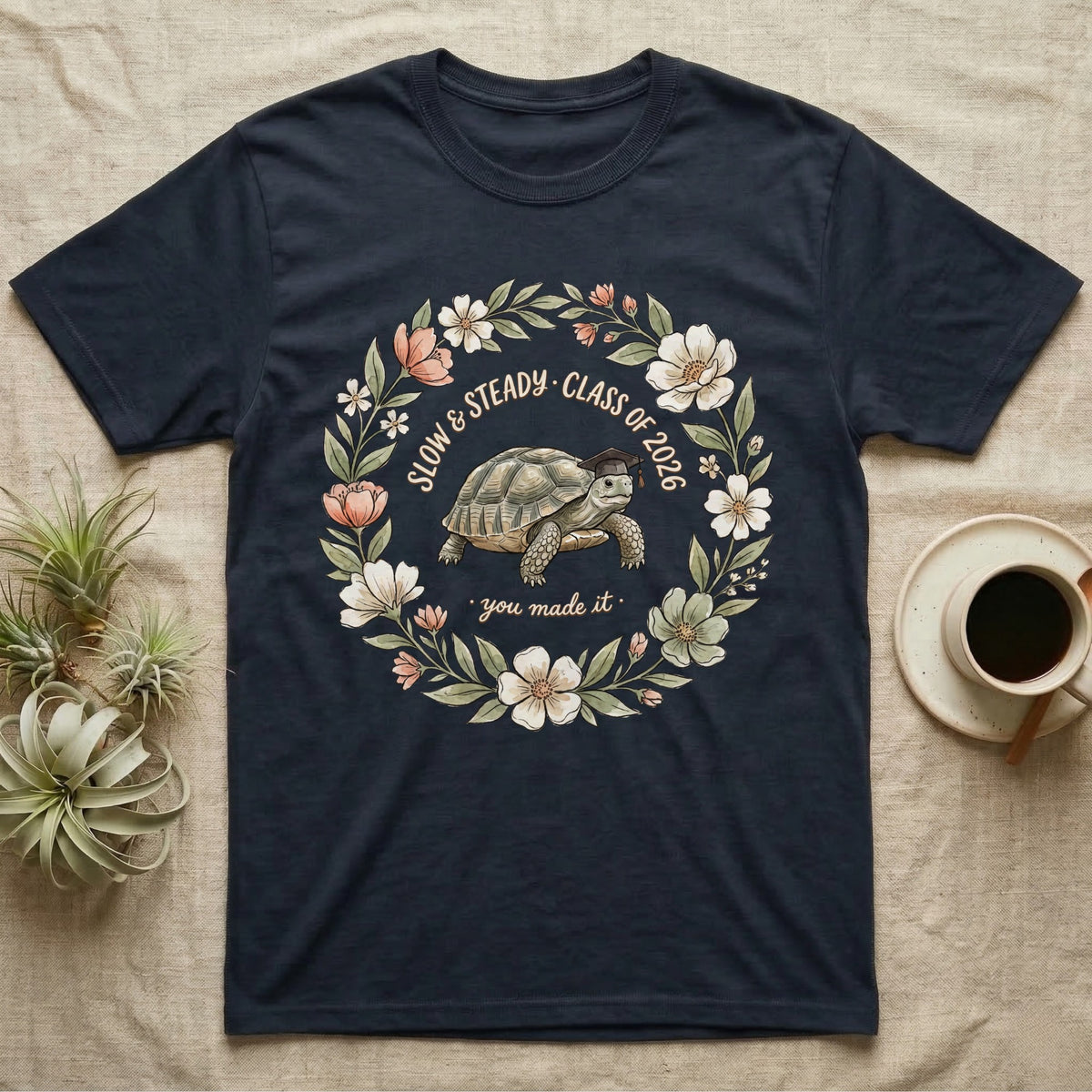 Slow And Steady Graduation T-Shirt in Navy — Watercolour illustration of a tortoise in a graduation cap inside a floral wreath with "Slow & Steady, Class of 2026."