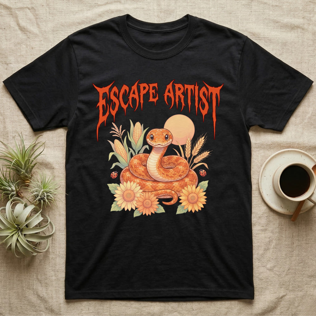 Corn Snake Feral T-Shirt in Black — Orange corn snake coiled in a pastel cornfield scene under a spiky blood-orange metal wordmark reading ESCAPE ARTIST.