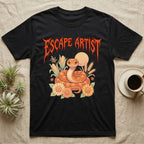 Corn Snake Feral T-Shirt in Black — Orange corn snake coiled in a pastel cornfield scene under a spiky blood-orange metal wordmark reading ESCAPE ARTIST.