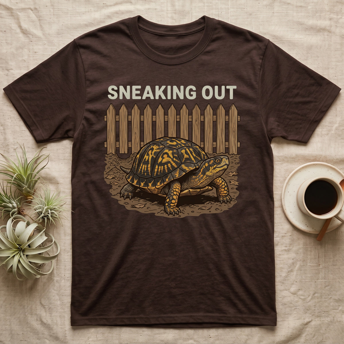 Box Turtle Sneaking T-Shirt in Dark Chocolate — Eastern box turtle crawling out from under a brown picket fence beneath the words Sneaking Out