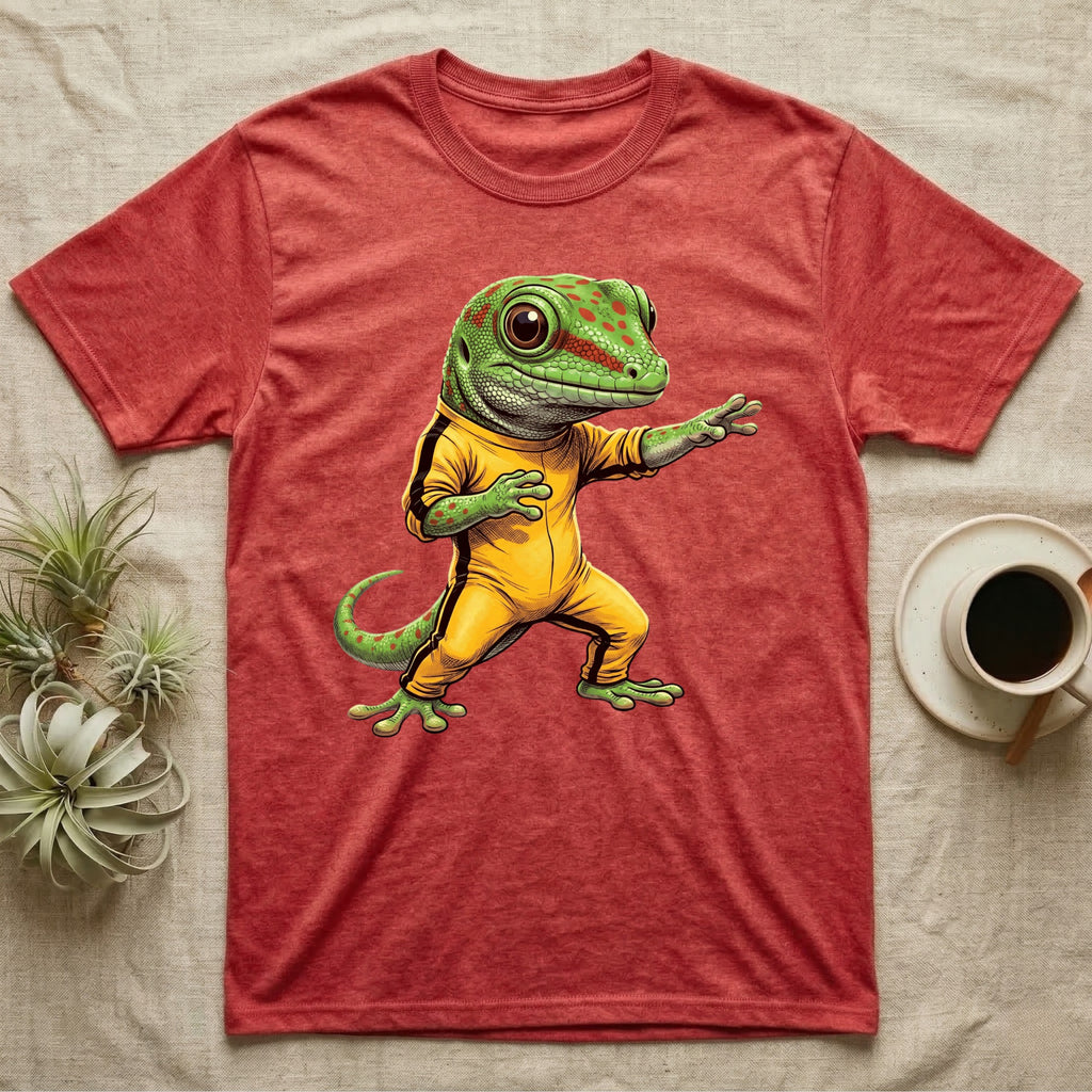 Anthropomorphic giant day gecko in a yellow-and-black martial-arts jumpsuit, low fighting stance, bold vintage-comic ink outlines and halftone shading, graphic-only design. — shown on a Heather Red tee.