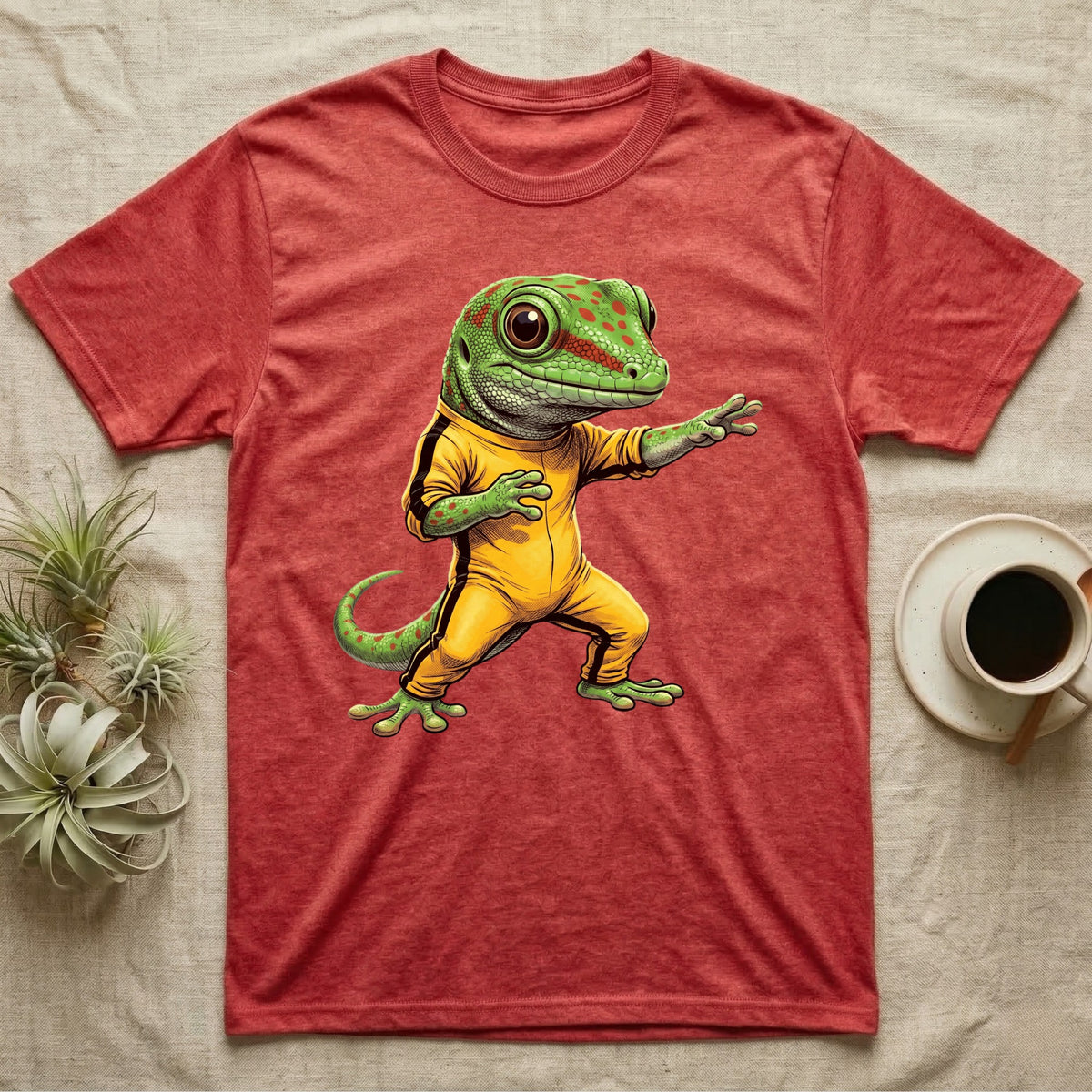 Anthropomorphic giant day gecko in a yellow-and-black martial-arts jumpsuit, low fighting stance, bold vintage-comic ink outlines and halftone shading, graphic-only design. — shown on a Heather Red tee.