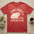 Tree Frog Proverb T-Shirt in Heather Red — Worn cream print of a dumpy White's tree frog catching a fly with its tongue under the words Zero Honey, Still Catching Flies