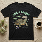 Red-Eared Slider Softie T-Shirt in Black — Red-eared slider turtle stretching its neck to beg, under pastel bubble text "just a beggar" with hearts.