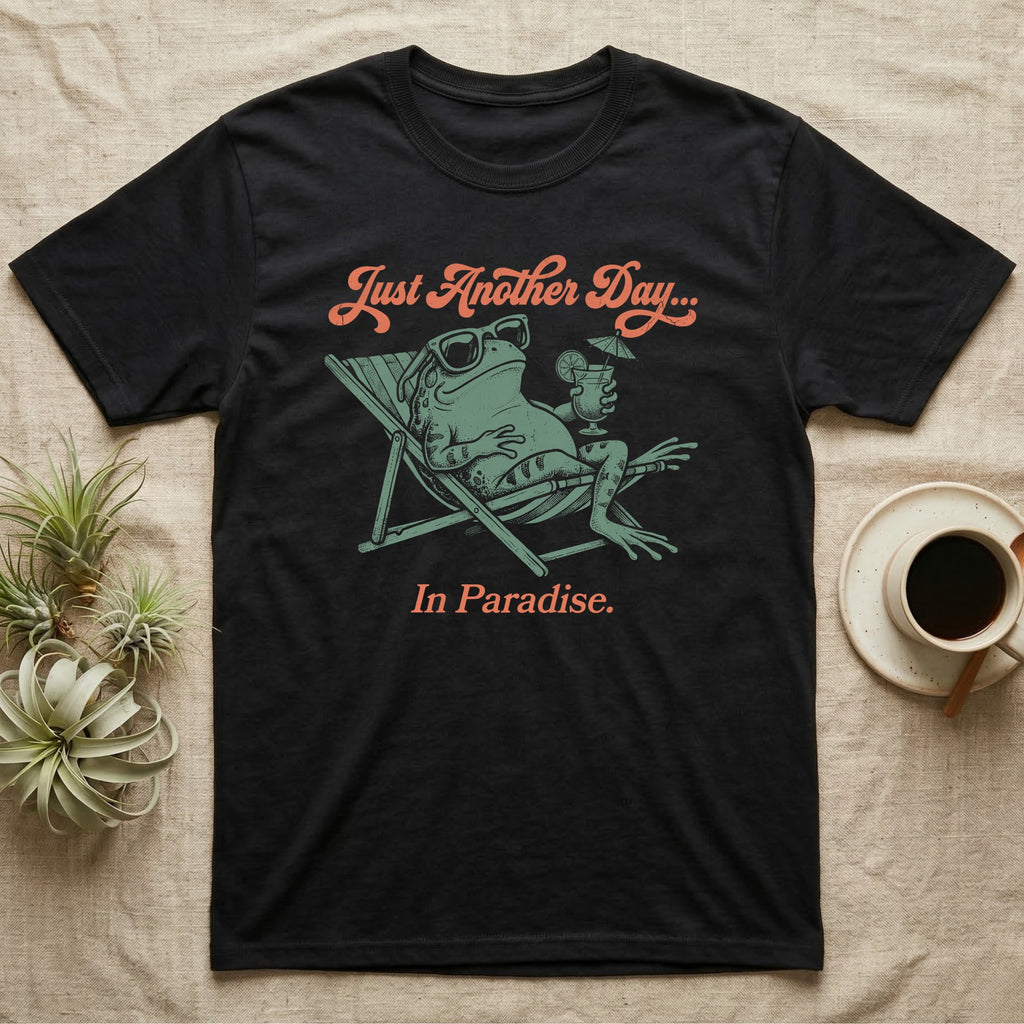 Fire-Bellied Toad Paradise T-Shirt in Black — Illustrated fire-bellied toad reclining in a beach chair with sunglasses and a cocktail, coral script reading Just Another Day In Paradise.