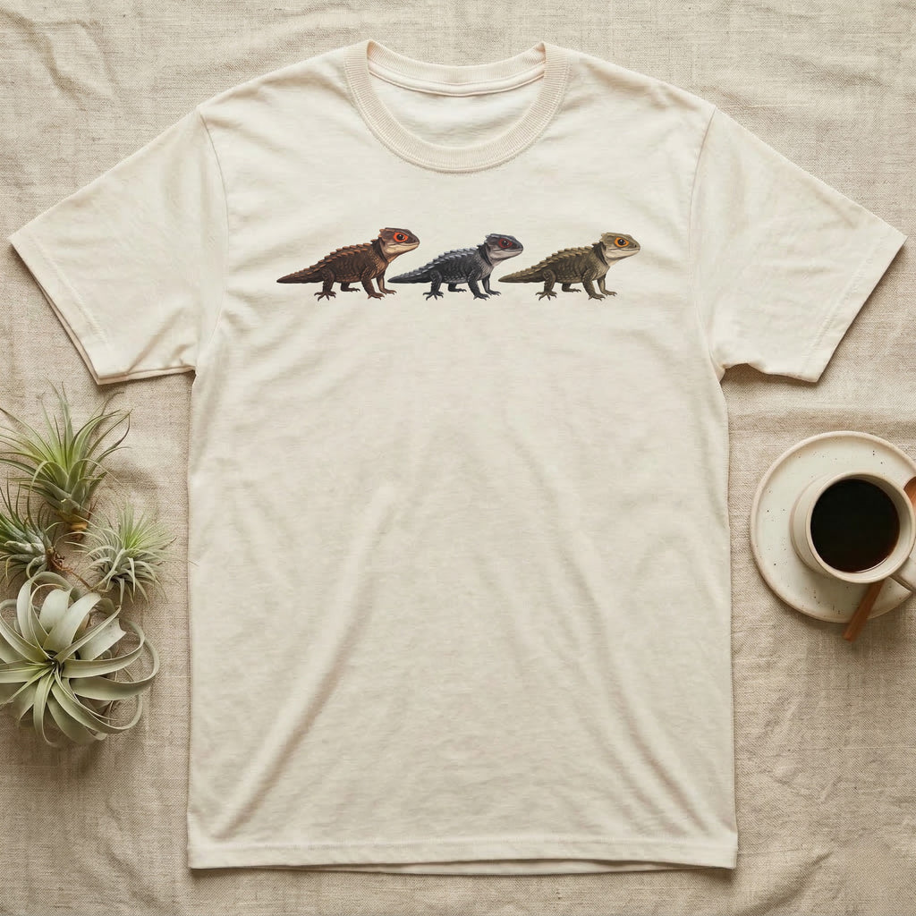 Crocodile Skink Morph Triptych T-Shirt in Natural — Three red-eyed crocodile skinks in a row, painted in thick impasto — bronze, near-black and pale olive forms.