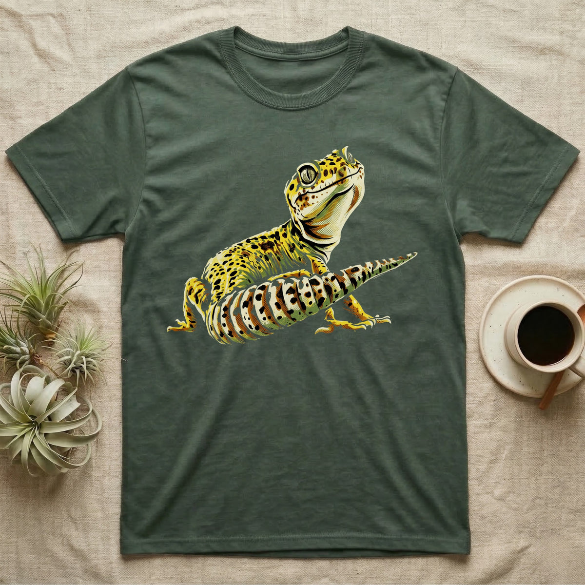 Illustration of a smiling leopard gecko with a plump curled spotted tail, bold vintage-comic ink outlines and halftone shading, graphic-only, no text. — shown on a Military Green tee.