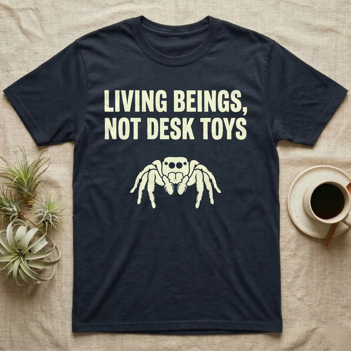 Living Beings Spider T-Shirt in Navy — Bold typographic broadside reading Living Beings Not Desk Toys above a small front-facing jumping spider silhouette.