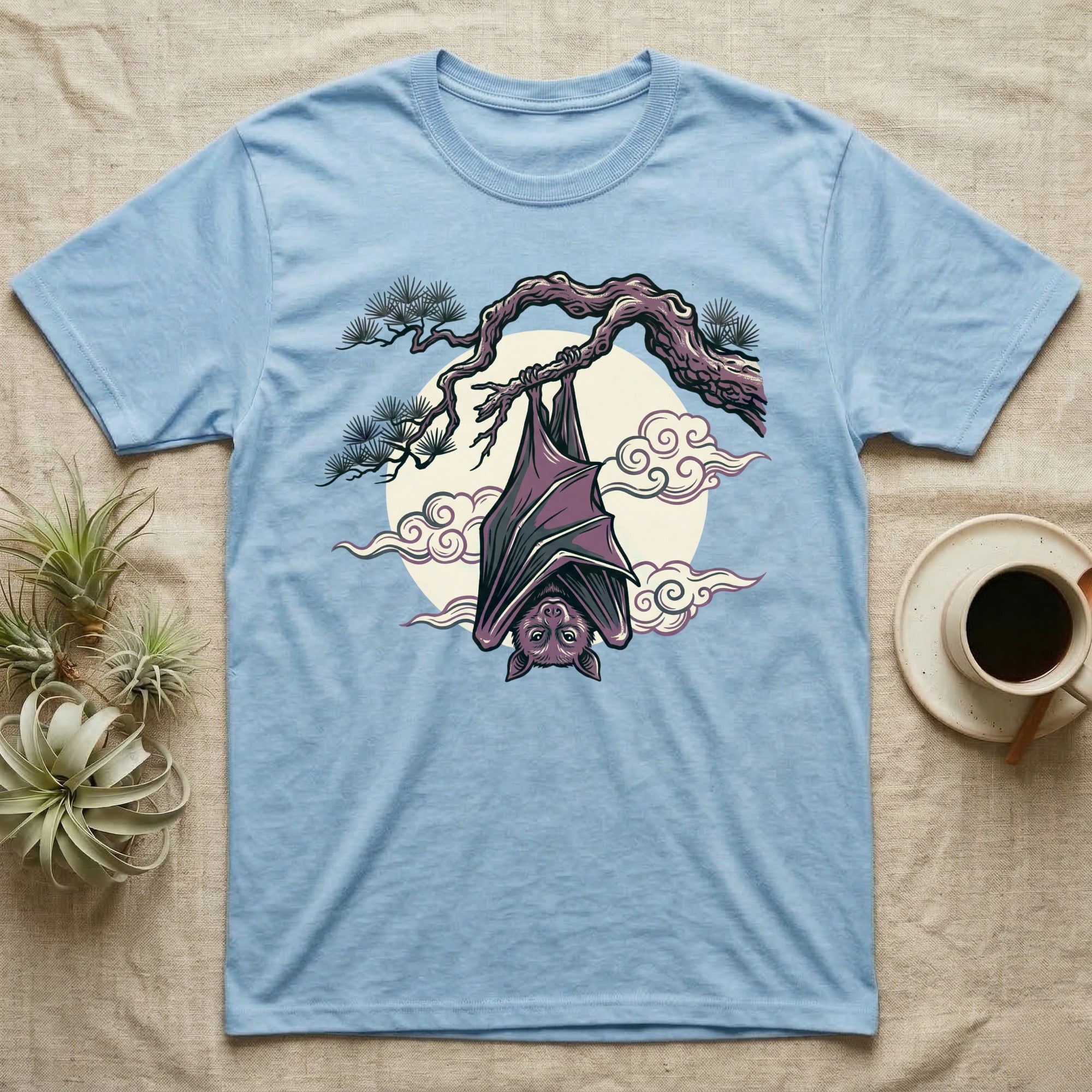 Light blue t-shirt featuring a hanging bat on a branch against a moon and clouds.