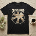 Macro badge illustration of a gecko's splayed foot with ribbed adhesive toe pads inside a distressed circular border, arched wordmark reading GECKO GRIP. — shown on a Black tee.