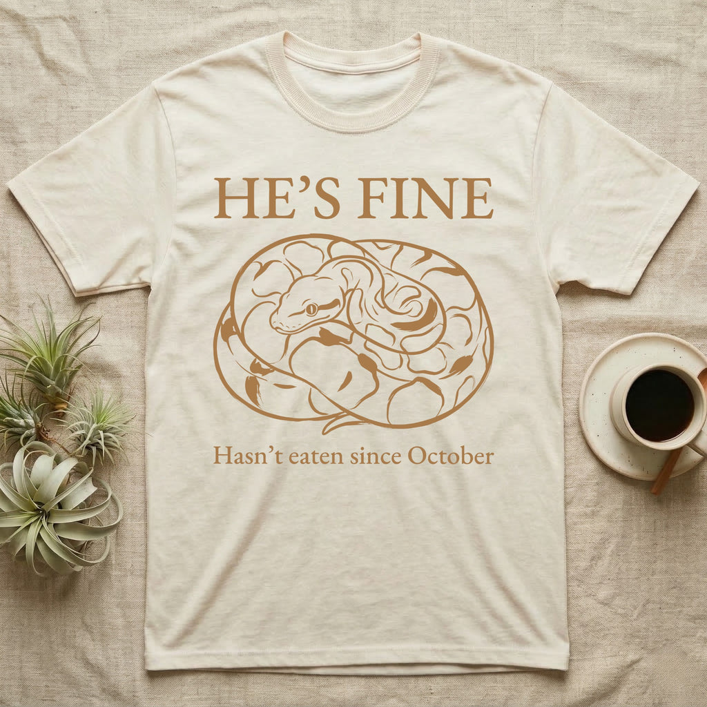 Ball Python He's Fine T-Shirt in Natural — One-ink linocut illustration of a ball python coiled into a tight defensive ball with "He's Fine" deadpan lettering above and below.