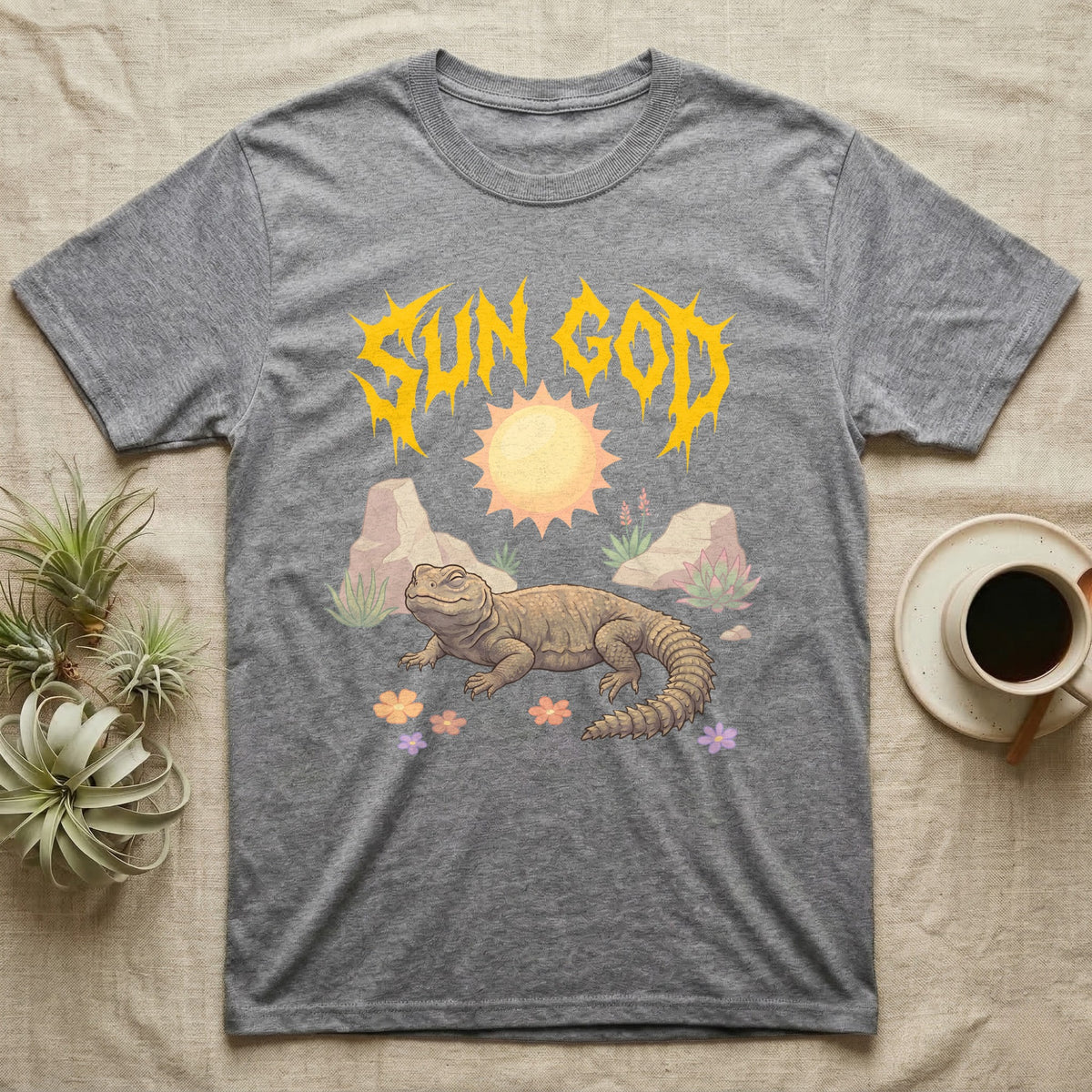 Moroccan Uromastyx Feral T-Shirt in Sport Grey — Moroccan uromastyx basking under a big sun with a jagged solar-gold metal "SUN GOD" wordmark and pastel desert scene.