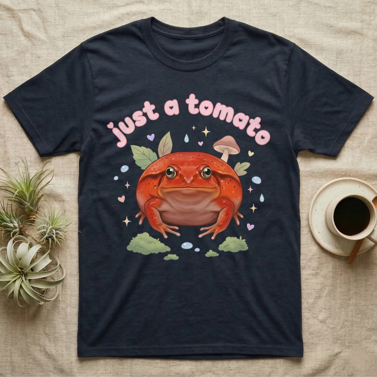 Tomato Frog Softie T-Shirt in Navy — Round red-orange tomato frog facing forward under a puffy pastel "just a tomato" bubble wordmark with tiny hearts.