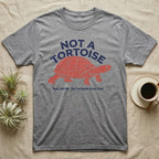 Box Turtle Not A Tortoise T-Shirt in Sport Grey — Two-ink worn stamp print of an eastern box turtle striding right on stumpy clawed legs beneath the arched words NOT A TORTOISE.