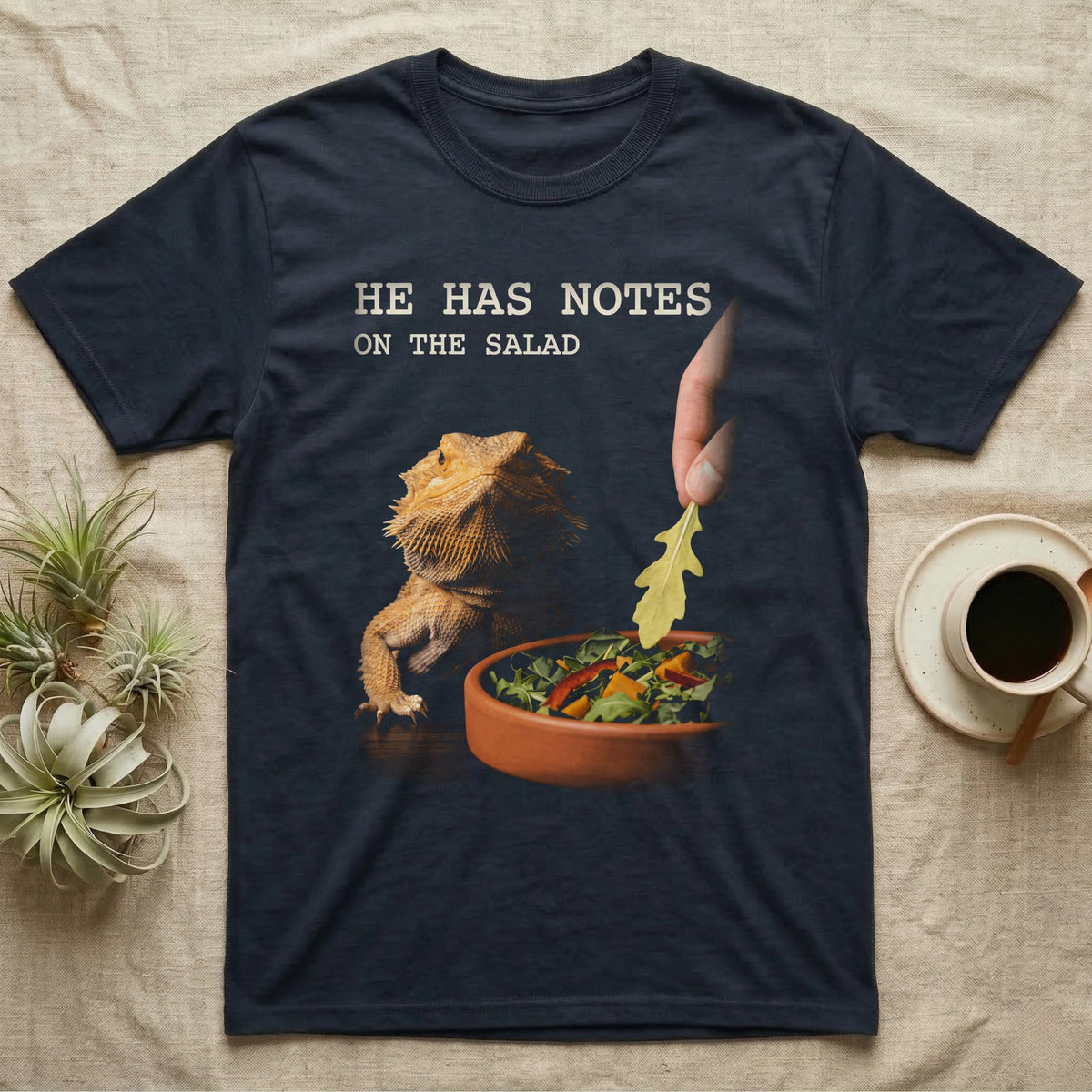 Bearded Dragon Salad Notes T-Shirt in Navy — Photorealistic bearded dragon staring flatly as a hand lowers an arugula leaf into a foreground salad dish.
