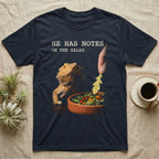 Bearded Dragon Salad Notes T-Shirt in Navy — Photorealistic bearded dragon staring flatly as a hand lowers an arugula leaf into a foreground salad dish.