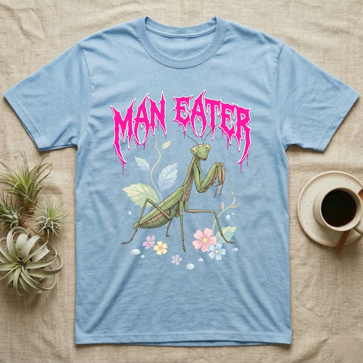 Chinese Mantis Feral T-Shirt in Light Blue — Pastel Chinese mantis with raised spiked forelegs among leaves and blossoms, jagged magenta metal wordmark "MAN EATER" above.