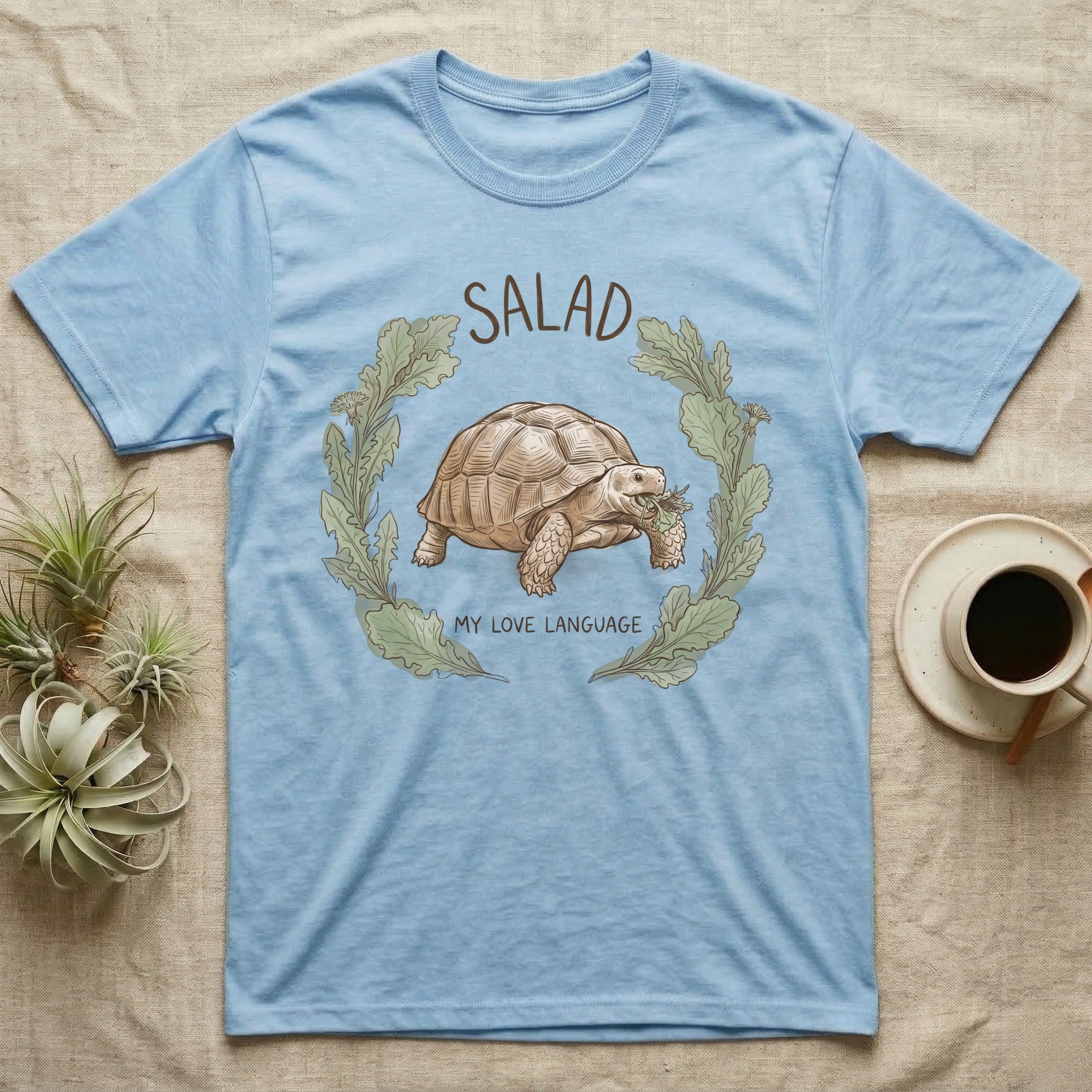Sulcata Tortoise Salad Love T-Shirt in Light Blue — Sepia watercolour illustration of a Sulcata tortoise mid-bite inside a salad-greens wreath with "SALAD" lettering.