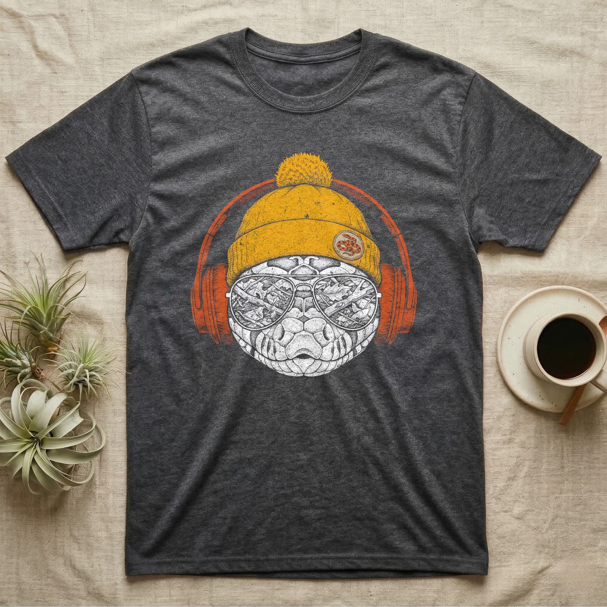 Corn Snake Chill Beats T-Shirt in Dark Heather — Engraved corn snake in a knit beanie and headphones, aviator lenses reflecting a leafy forest floor.