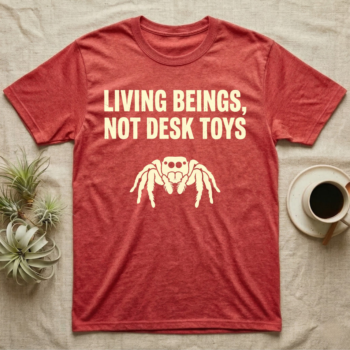 Living Beings Spider T-Shirt in Heather Red — Bold typographic broadside reading Living Beings Not Desk Toys above a small front-facing jumping spider silhouette.