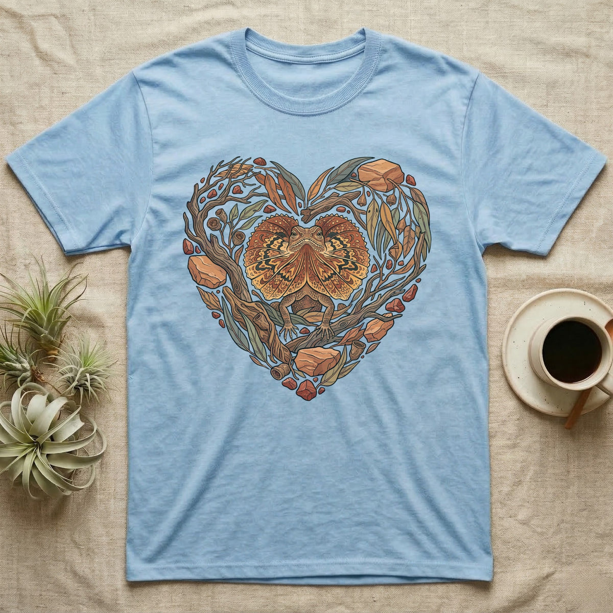 Light blue t-shirt with a heart-shaped illustration of a frilled lizard among leaves and branches.