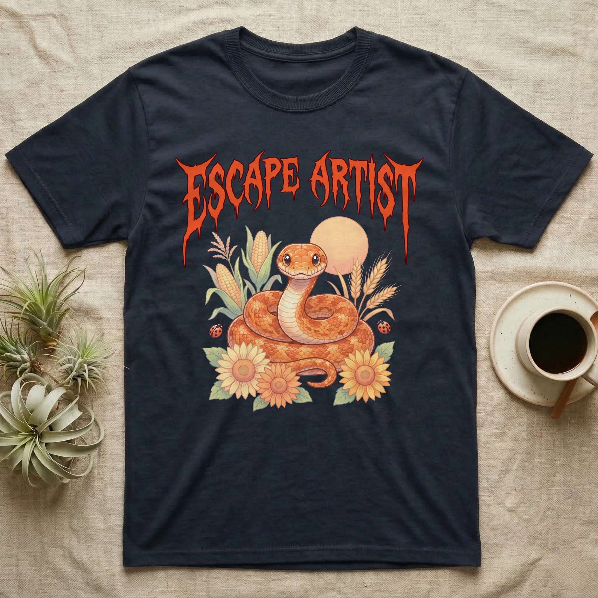 Corn Snake Feral T-Shirt in Navy — Orange corn snake coiled in a pastel cornfield scene under a spiky blood-orange metal wordmark reading ESCAPE ARTIST.