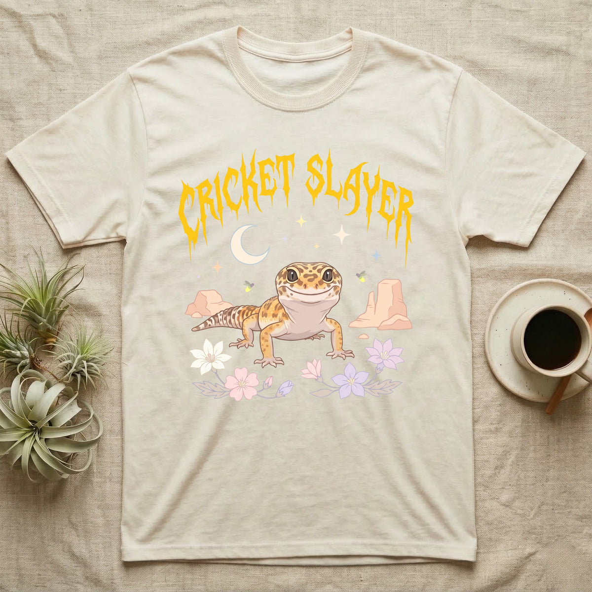Leopard Gecko Feral T-Shirt in Natural — Smiling leopard gecko in a pastel desert-night scene under a spiky golden metal wordmark reading CRICKET SLAYER.