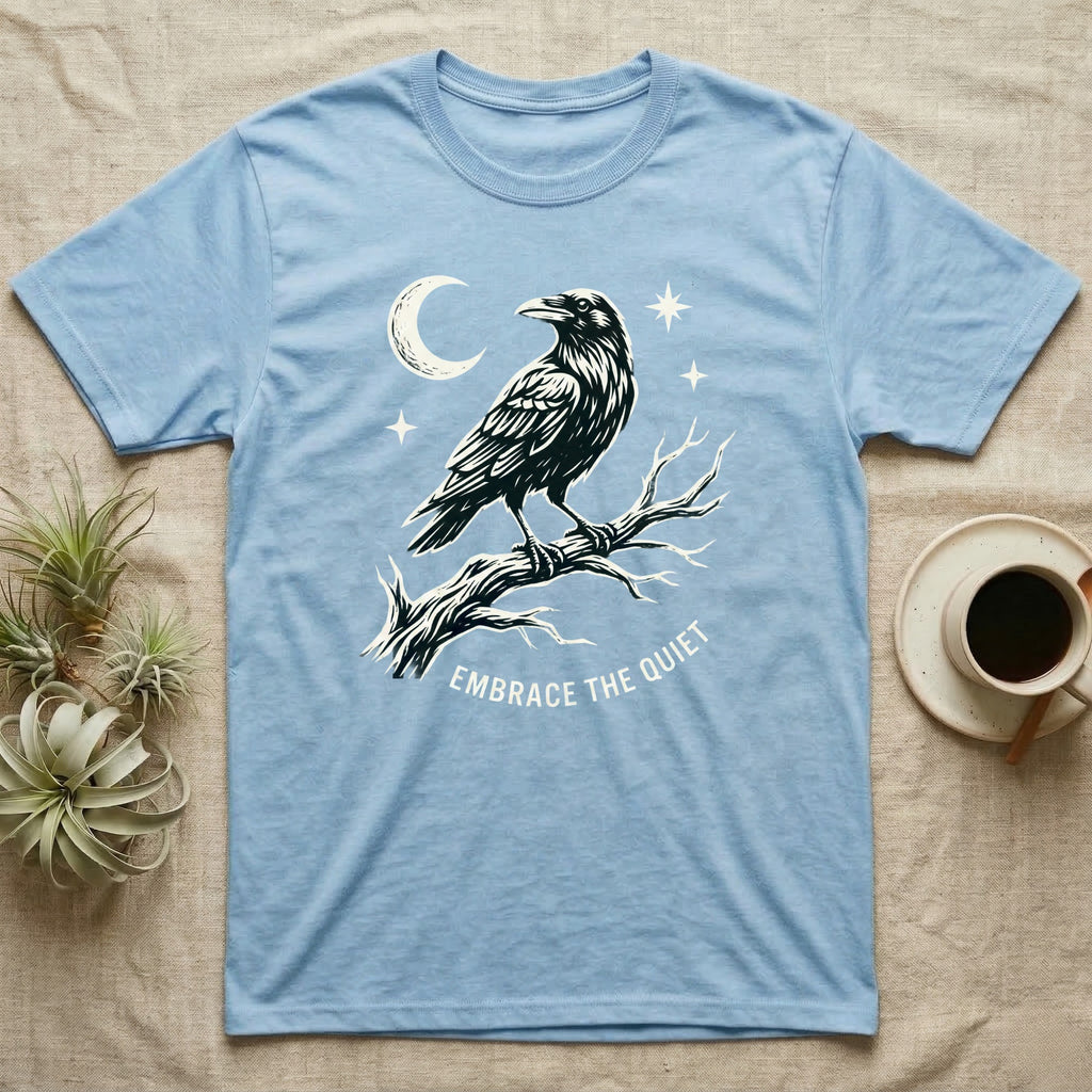Light blue t-shirt with a crow on a branch, moon, stars, and text "EMBRACE THE QUIET".