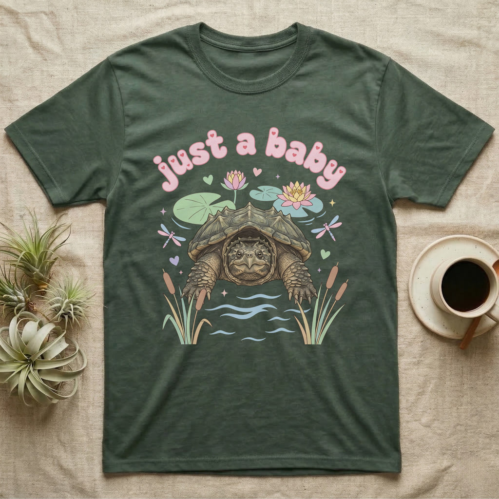 Common Snapping Turtle Baby T-Shirt in Military Green — Snapping turtle with hooked beak and spiky shell among pastel lily pads under puffy pink bubble text "just a baby".